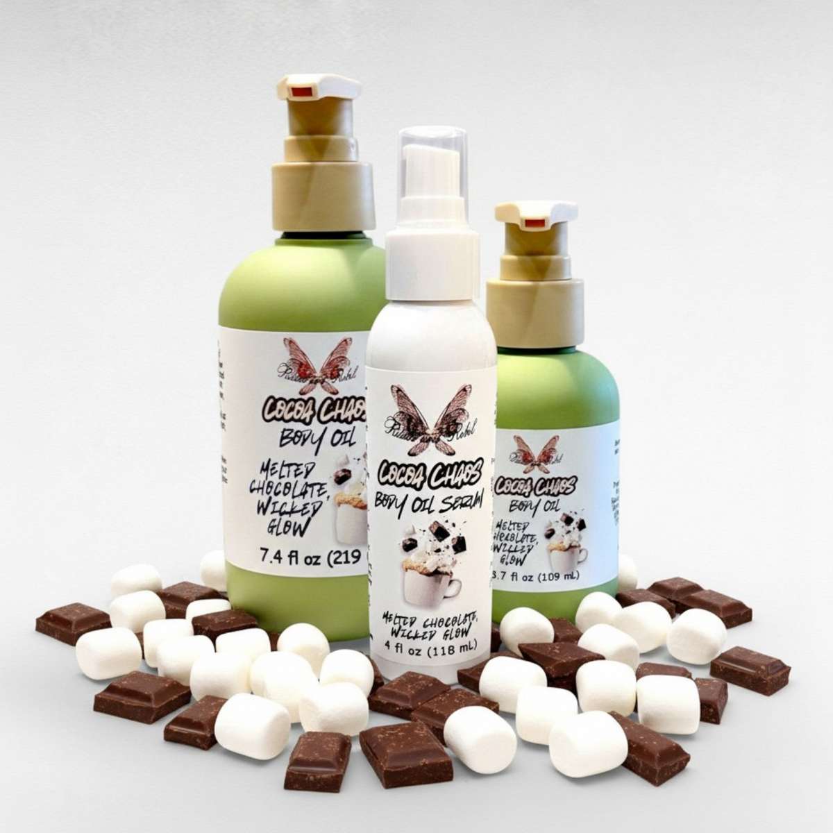 Cocoa Chaos Body Oil by Ritual and Rebel 2 green bottles 7.4 and 3.7 fl oz and 1 white bottle 4 fl oz with marshmallows and chocolate around bottom of jars