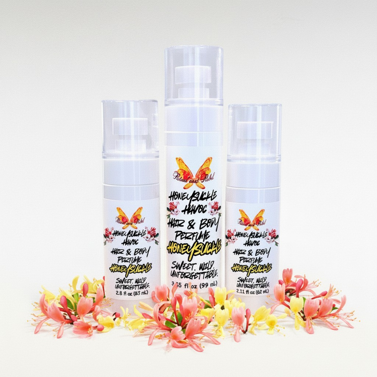 Three bottles of Honeysuckle Hair & Body Perfume 'Honeysuckle Havoc' arranged together on a white background, decorated with pink and yellow flowers at the base.