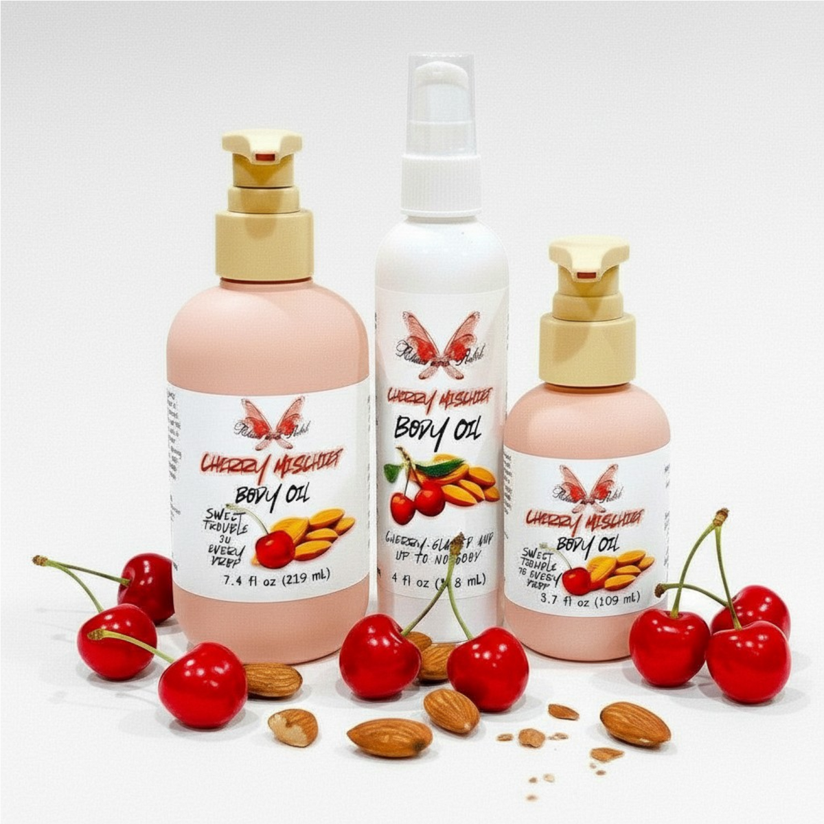 Cherry Mischief Body Oil by Ritual and Rebel 3 bottles of 7.4, 4, and 3.7 fl oz with cherry and almonds by base of bottles 