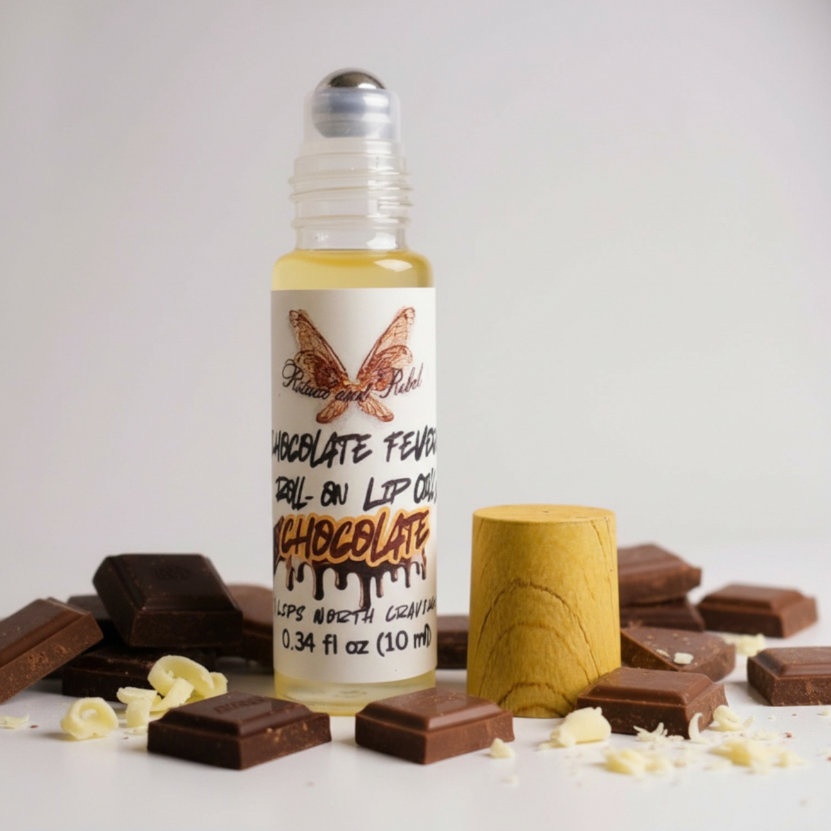 Chocolate Fever Lip Oil by Ritual and Rebel Roll-on lip oil with chocolate flavor packaging on a white background with chocolate pieces.