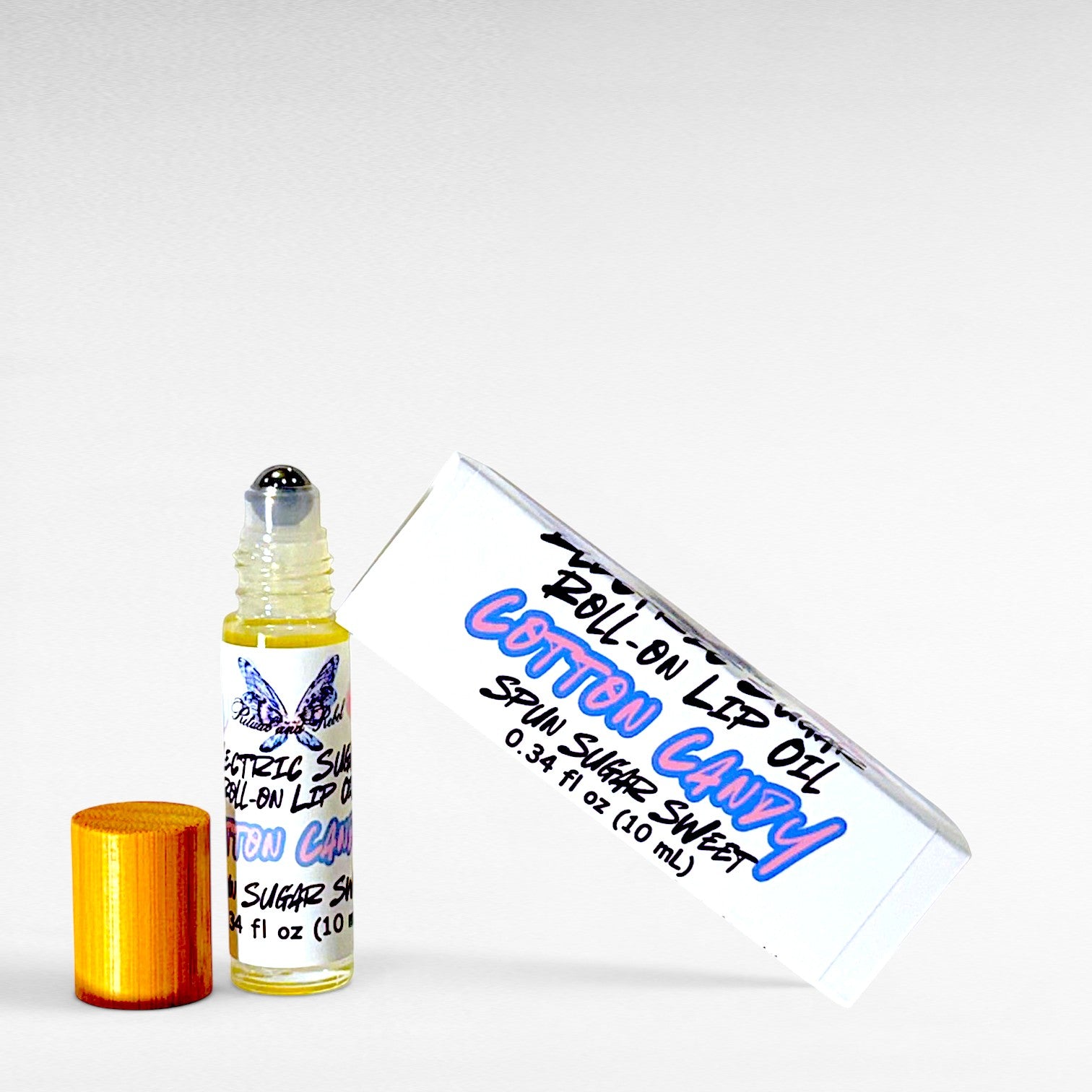 Electric Sugar cotton candy roll-on lip oil by Ritual and Rebel with glossy pink candy-inspired aesthetic on a white background with white logo product box and bamboo wood top