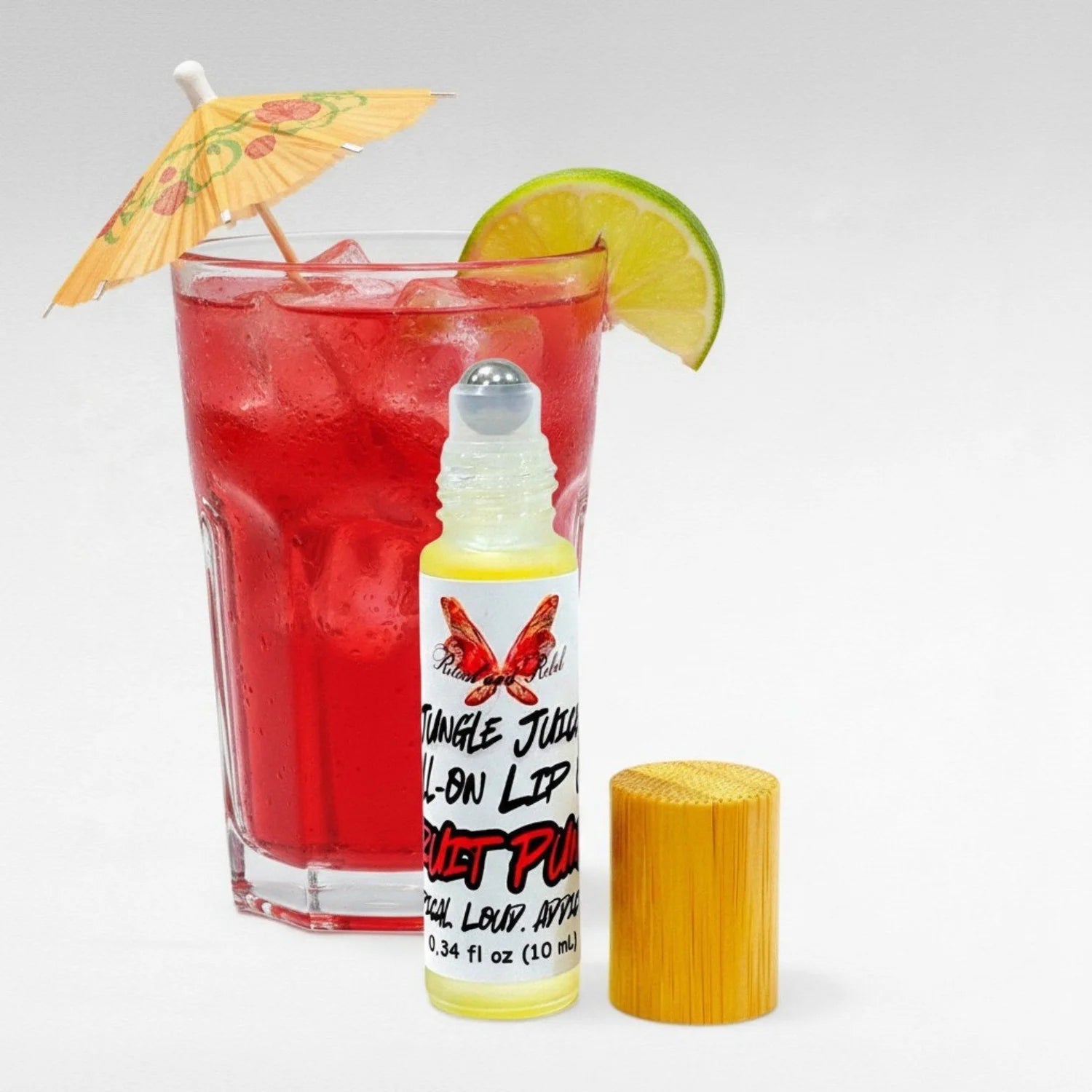 Jungle Juice Roll-On Lip Oil by Ritual and Rebel natural lip oil in glass bottle with bamboo top, fruit punch drink with little umbrella in background 10ml